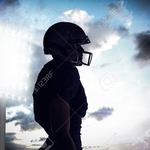 Side view of silhouette American football player standing against spotlight in sky